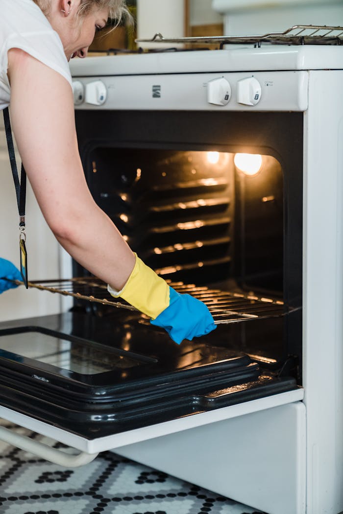 Adult woman cleaning an oven using protective rubber gloves indoors.